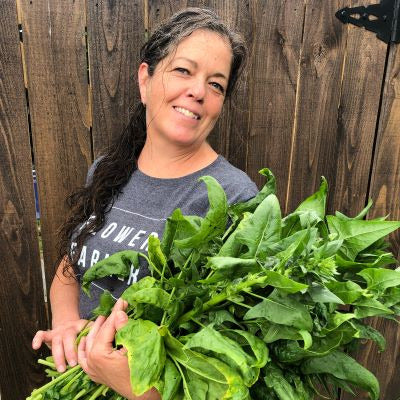 Woman holding a large bunch of fresh greens against a wooden fence.