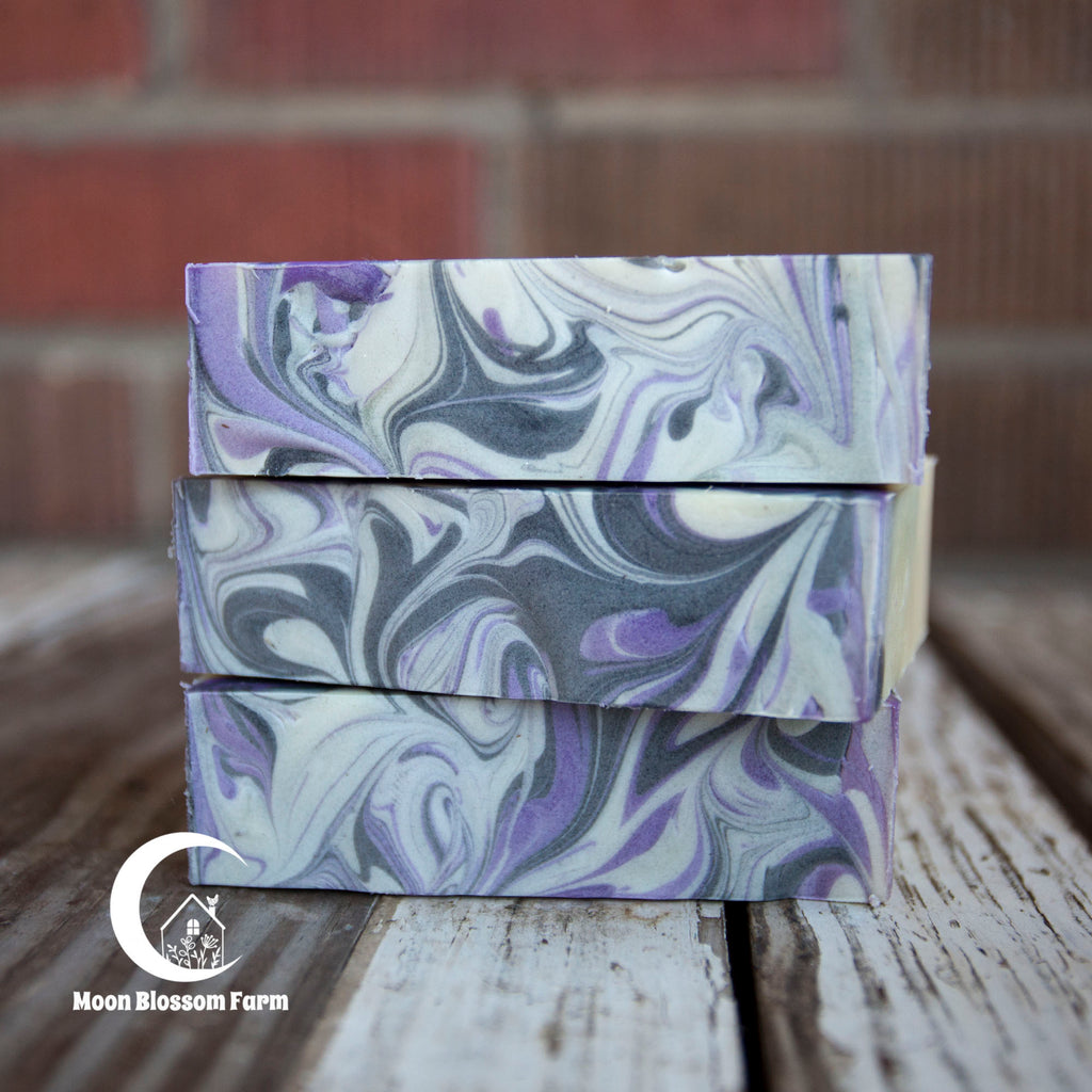 Three bars of marbled soap stacked on a wooden surface with a brick wall background.