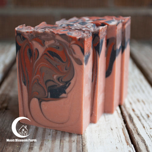 Four bars of marbled soap on a wooden surface with 'Moon Blossom Farm' branding.