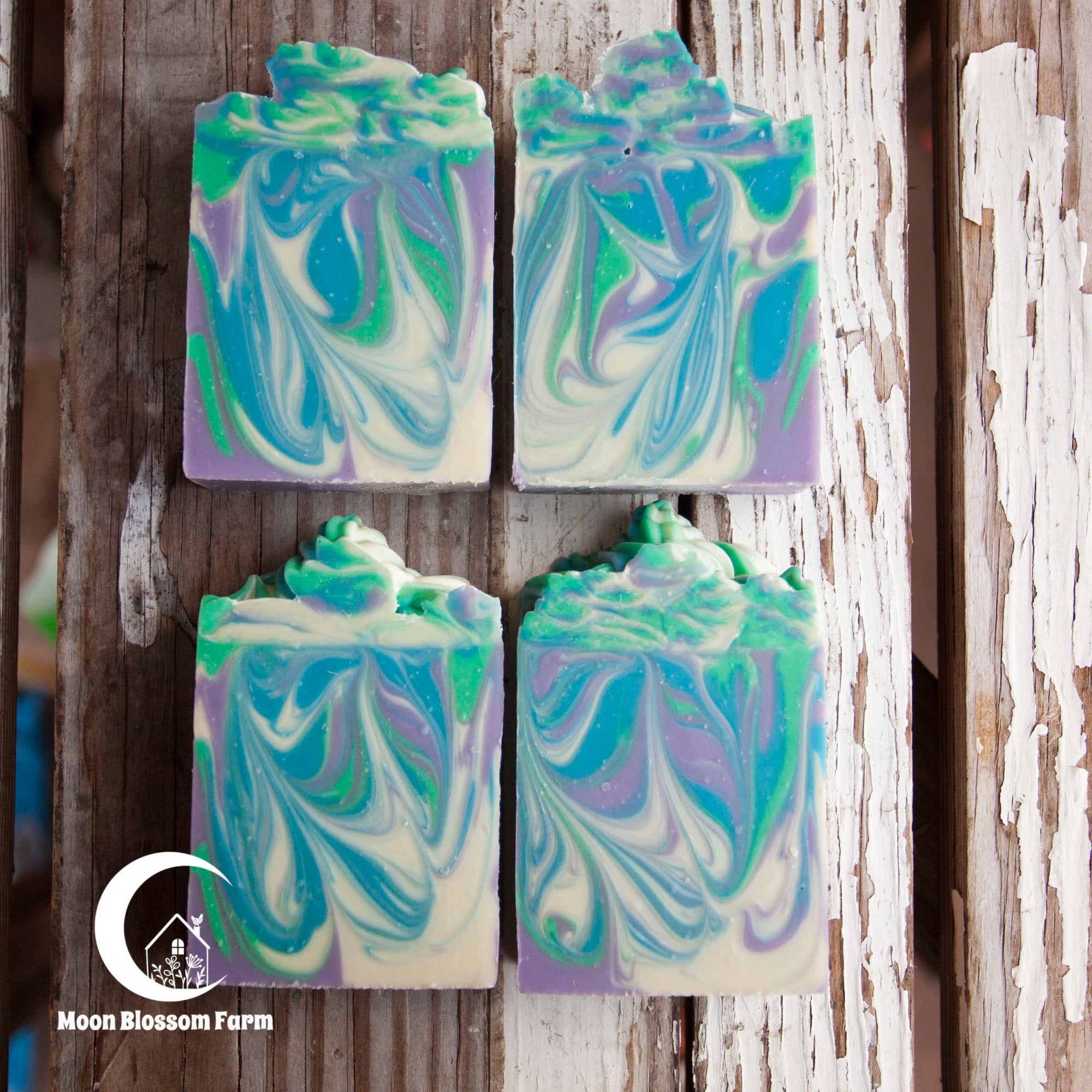 Four bars of marbled soap in green, blue, and purple on a wooden background with 'Moon Blossom Farm' logo.