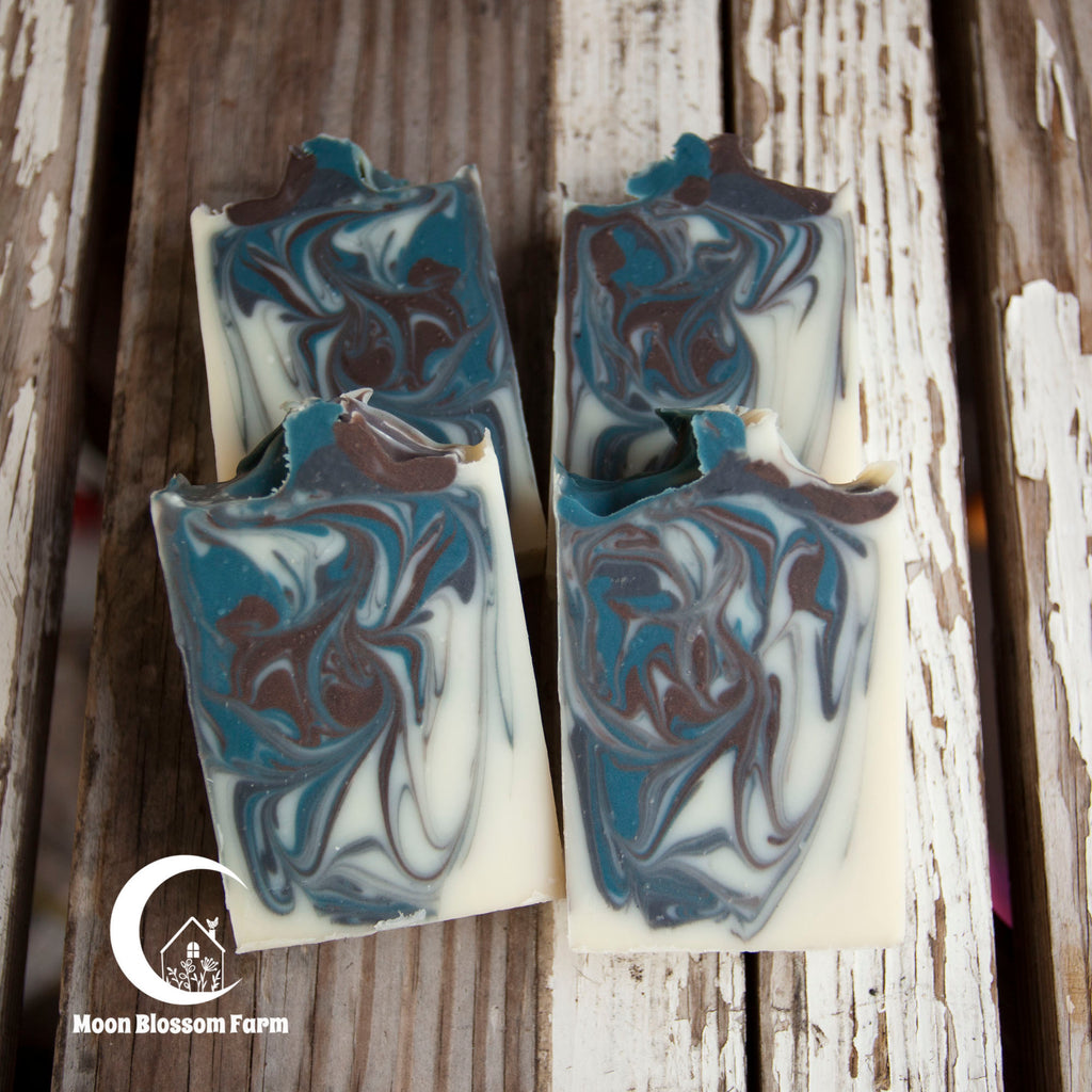 Marbled soap bars on a rustic wooden background with Moon Blossom Farm logo.