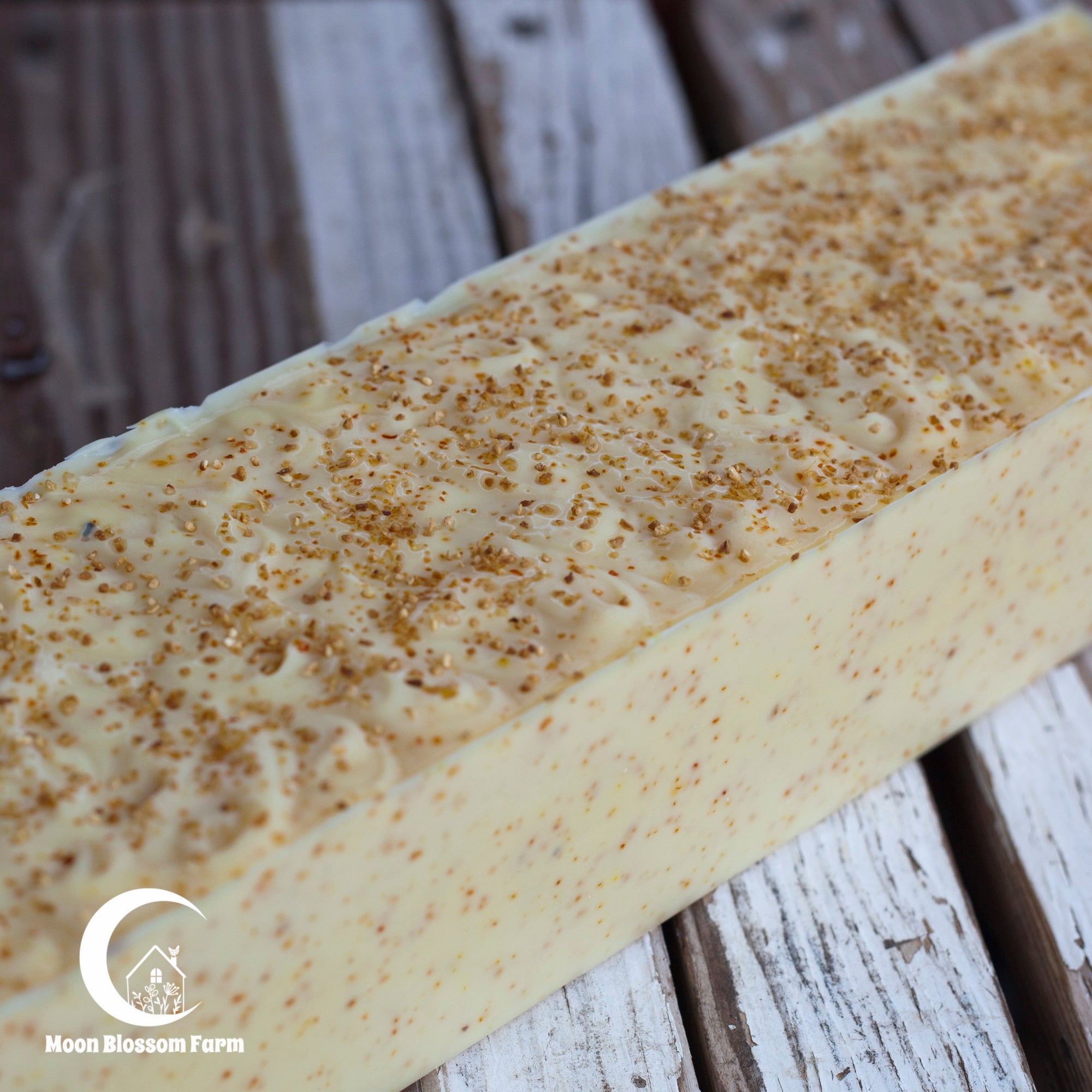 Block of soap with lemon peel on a wooden surface, branded 'Moon Blossom Farm'.