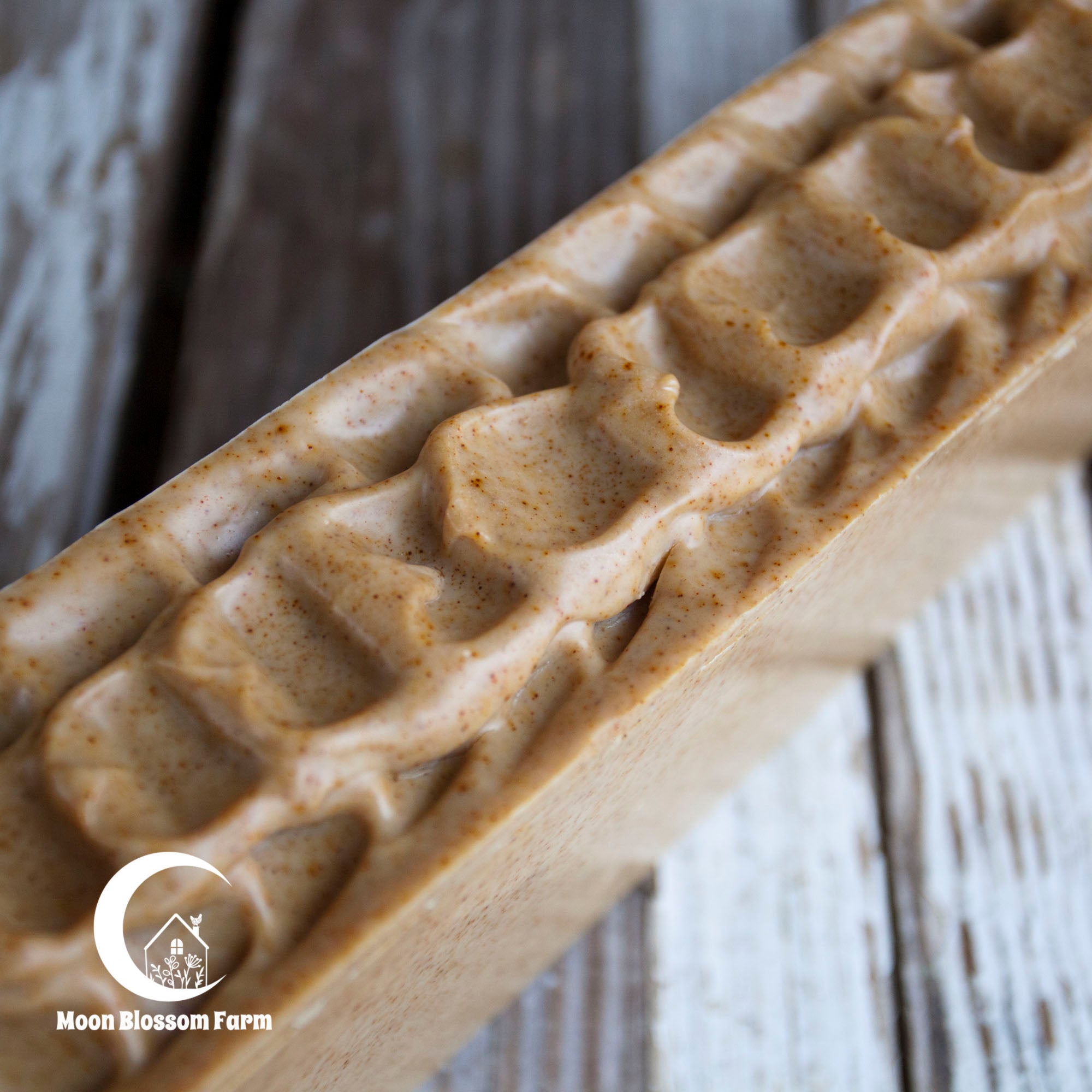 Loaf of soap with waffle pattern on a wooden surface, branded 'Moon Blossom Farm'.