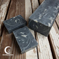 Three bars of black and white swirled soap on a wooden surface with Moon Blossom Farm logo.