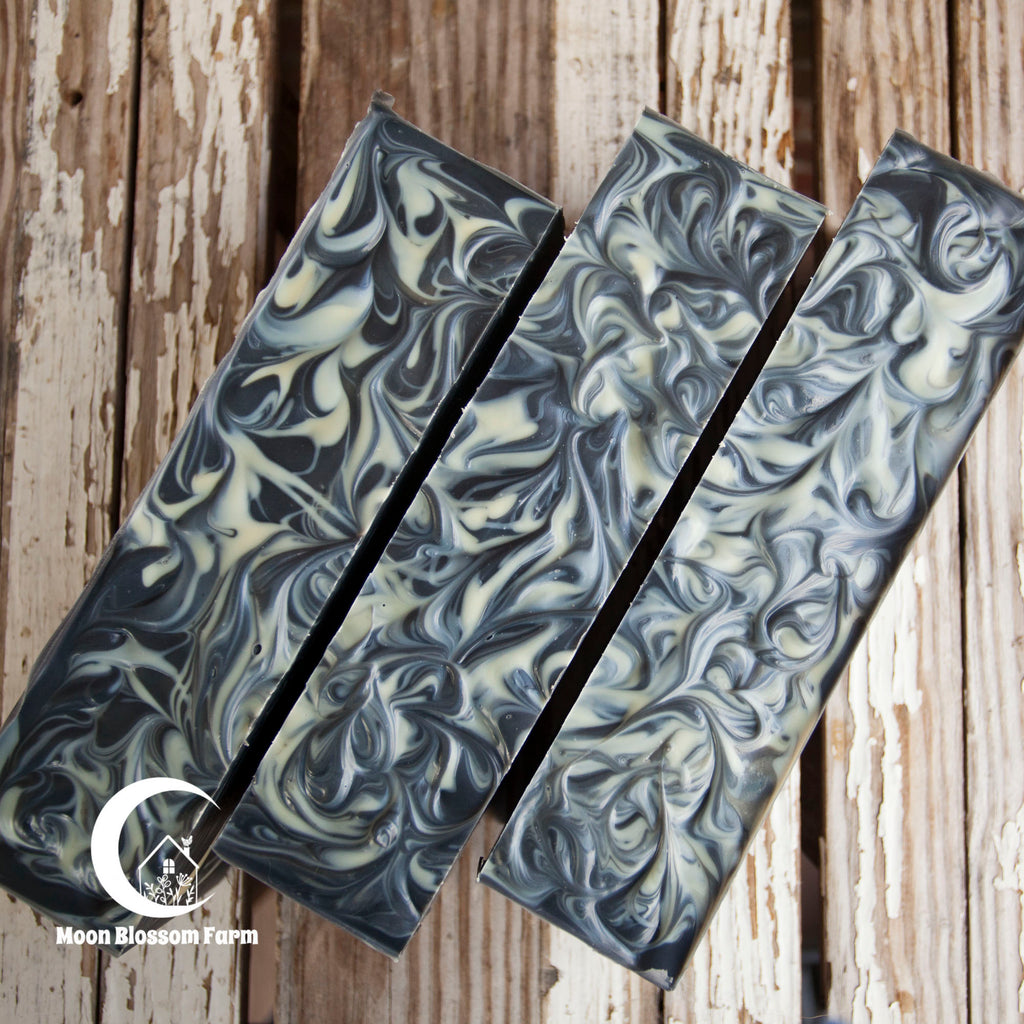 Three loaves of marbled soap on a wooden background with 'Moon Blossom Farm' branding.