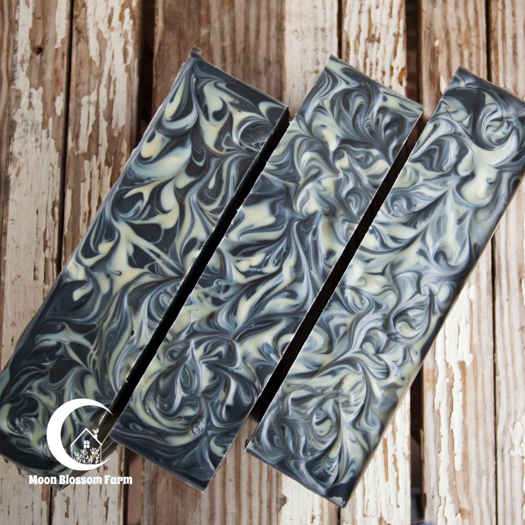 Three loaves of marbled soap on a wooden background with 'Moon Blossom Farm' branding.