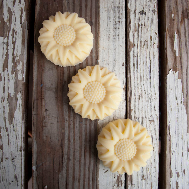 Three flower-shaped soap bars on a wooden surface